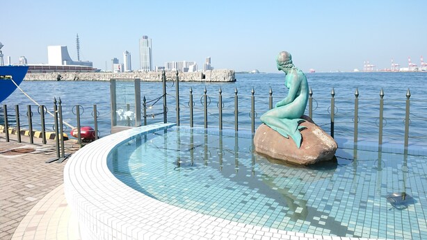 Una estatua de sirena en una piscina, con un paisaje urbano al fondo.