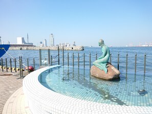 Eine Meerjungfernstatue in einem Pool mit Stadtansicht im Hintergrund.