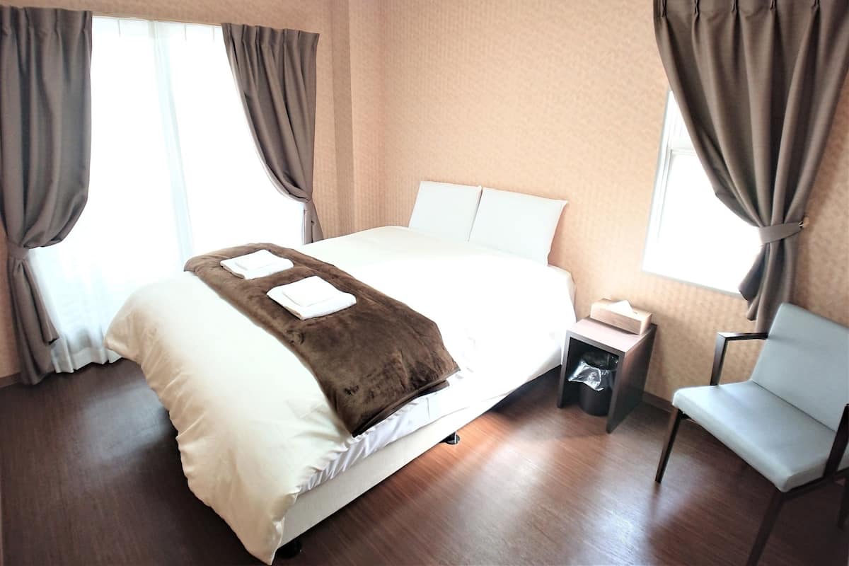 Une chambre d’hôtel avec un grand lit, une chaise, une table de chevet et une fenêtre avec des rideaux.
