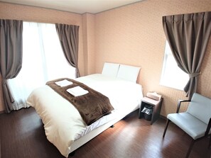 Ein Hotelzimmer mit einem großen Bett, einem Sessel, einem Nachttisch und einem Fenster mit Vorhängen.