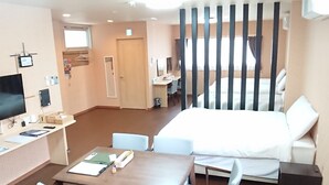 Habitación de hotel con cama, escritorio con computadora, televisor y zona de comedor con sillas y mesa.