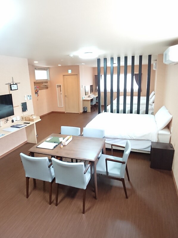Ein Hotelzimmer mit einem Bett, einem Schreibtisch mit Computer, einem Fernseher und einer Essecke mit Stühlen und Tisch.