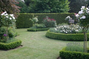 Un jardín cuidado con setos podados, diversas plantas en flor y un parterre circular.