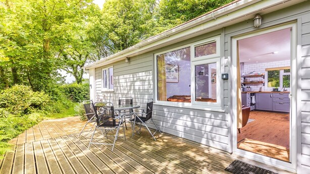 Ein Haus mit einer Terrasse, einem Essbereich mit Stühlen und einer durchgehenden Tür erkennbaren Küche.