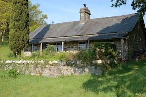A stone house with a sloped roof, a chimney, and a stone wall in front.