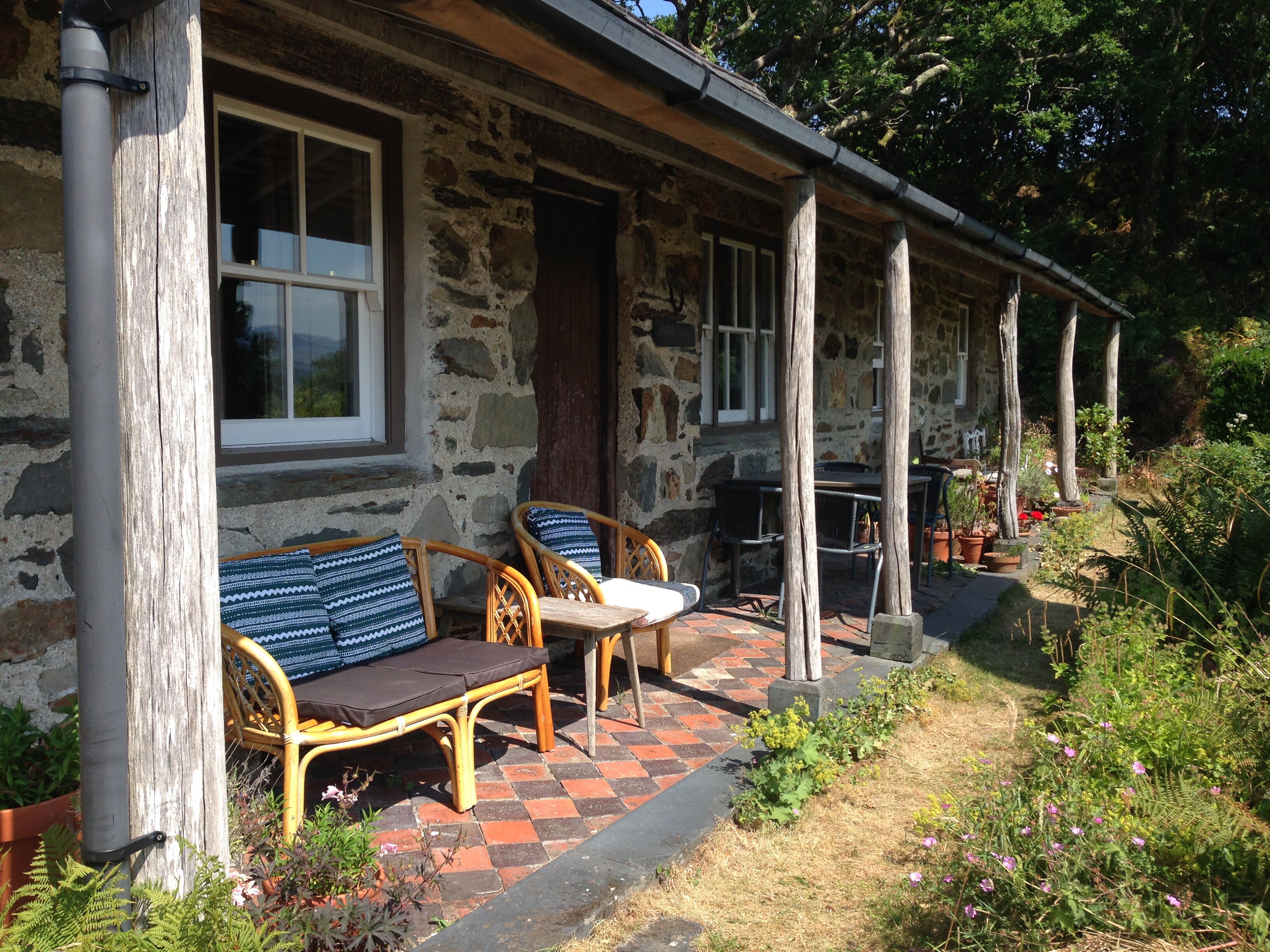 A stone building with a porch, wicker furniture, and potted plants.