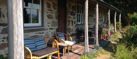 A stone building with a porch, wicker furniture, and potted plants.