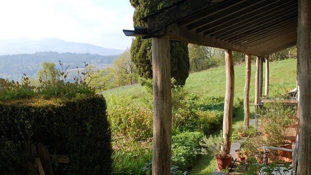 Una pérgola de madera con vistas a un jardín exuberante y montañas distantes.