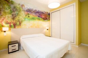 Un dormitorio con cama, mesita de noche y un mural abstracto y colorido en la pared.