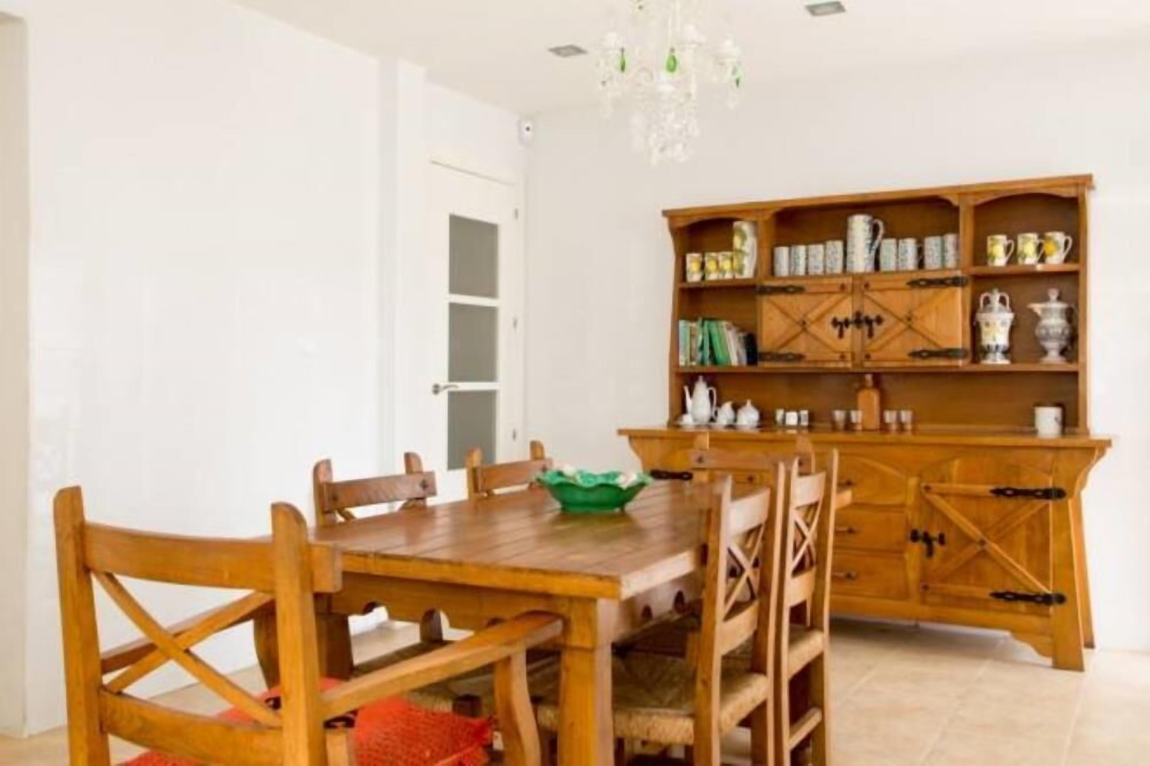 A dining area with a wooden table and chairs, a green bowl, and a wooden cabinet with kitchenware.