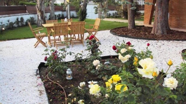 Ein Außenbereich mit Holzbänken und einem Tisch, umgeben von einem Garten mit verschiedenen Blumen.