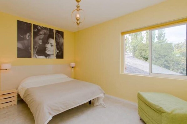A bedroom with a bed, a bench, a window with a view, and wall art.