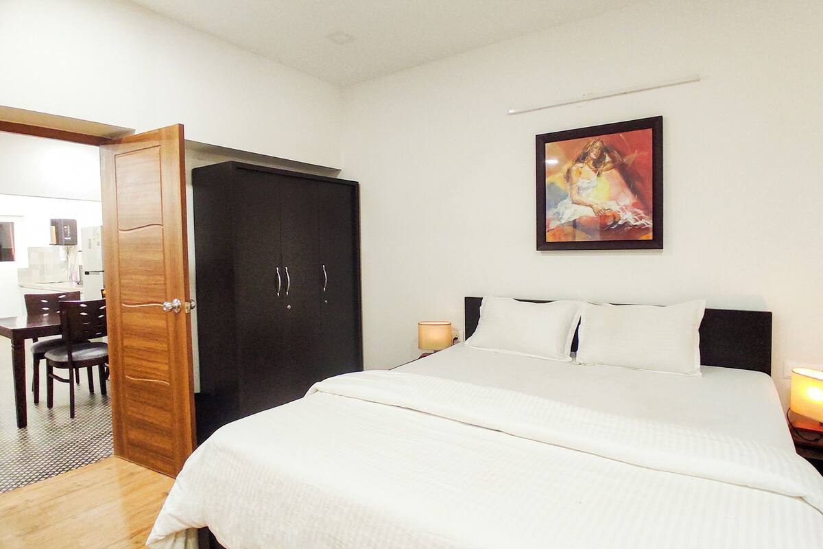 A bedroom with a bed, bedside lamps, a wardrobe, and a painting on the wall.