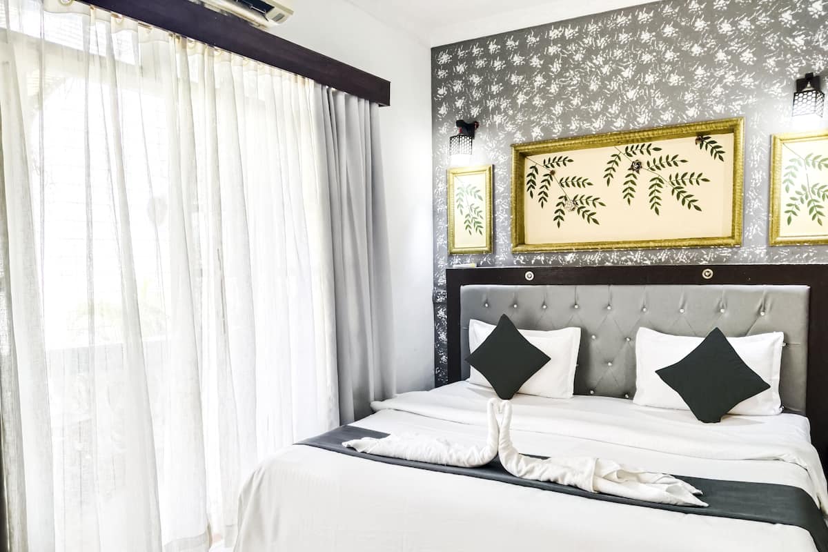 A hotel room with a large bed, white bedding, a grey headboard, and floral wall art.