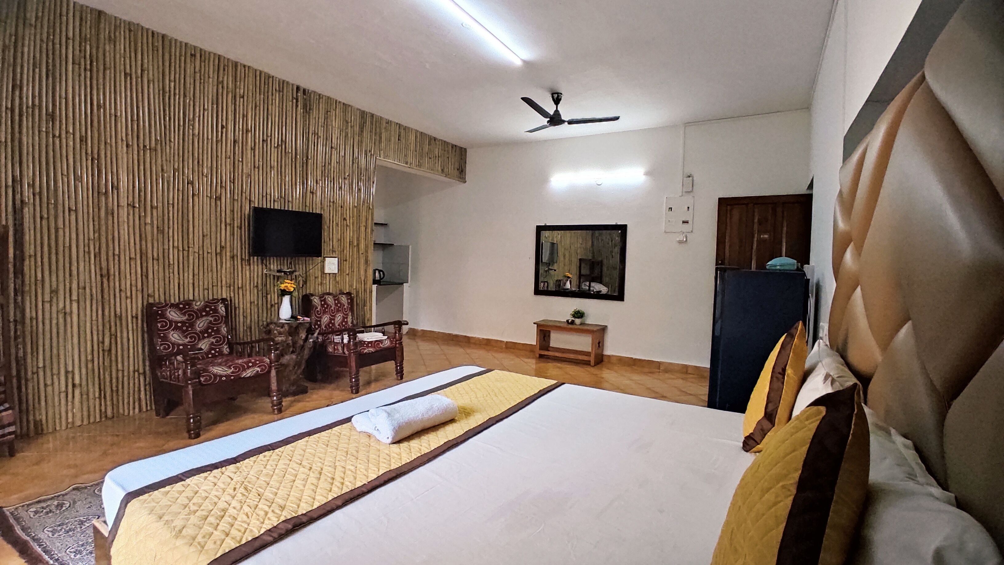 A hotel room with a bed, a TV, a ceiling fan, a mirror, and a wooden wall.