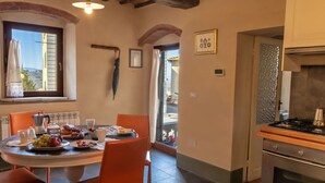 Ein Essbereich mit einem runden Tisch, orangefarbenen Stühlen und Blick ins Freie durch ein Fenster.