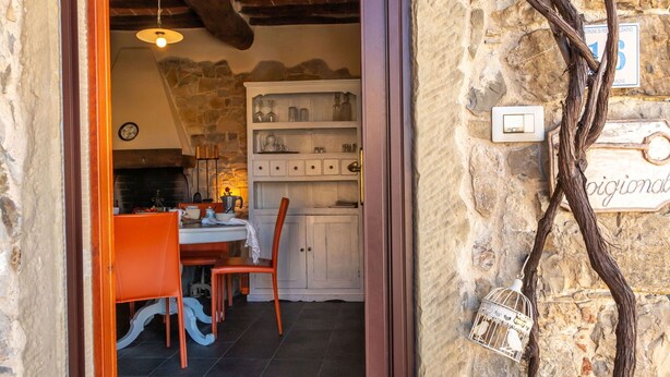 Ein rustikales Interieur mit einer Steinwand, Holzbalken, einem Essbereich mit orangefarbenen Stühlen und einem weißen Schrank mit Gläsern.