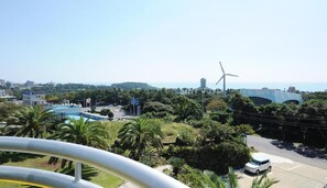 A coastal cityscape with a wind turbine, a swimming pool, and lush greenery.