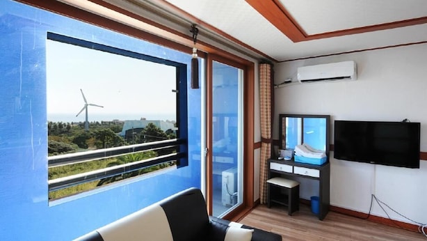 A room with a large window, a flat-screen TV, a desk, and a chair. - Dream & Green Pension (Seogwipo)