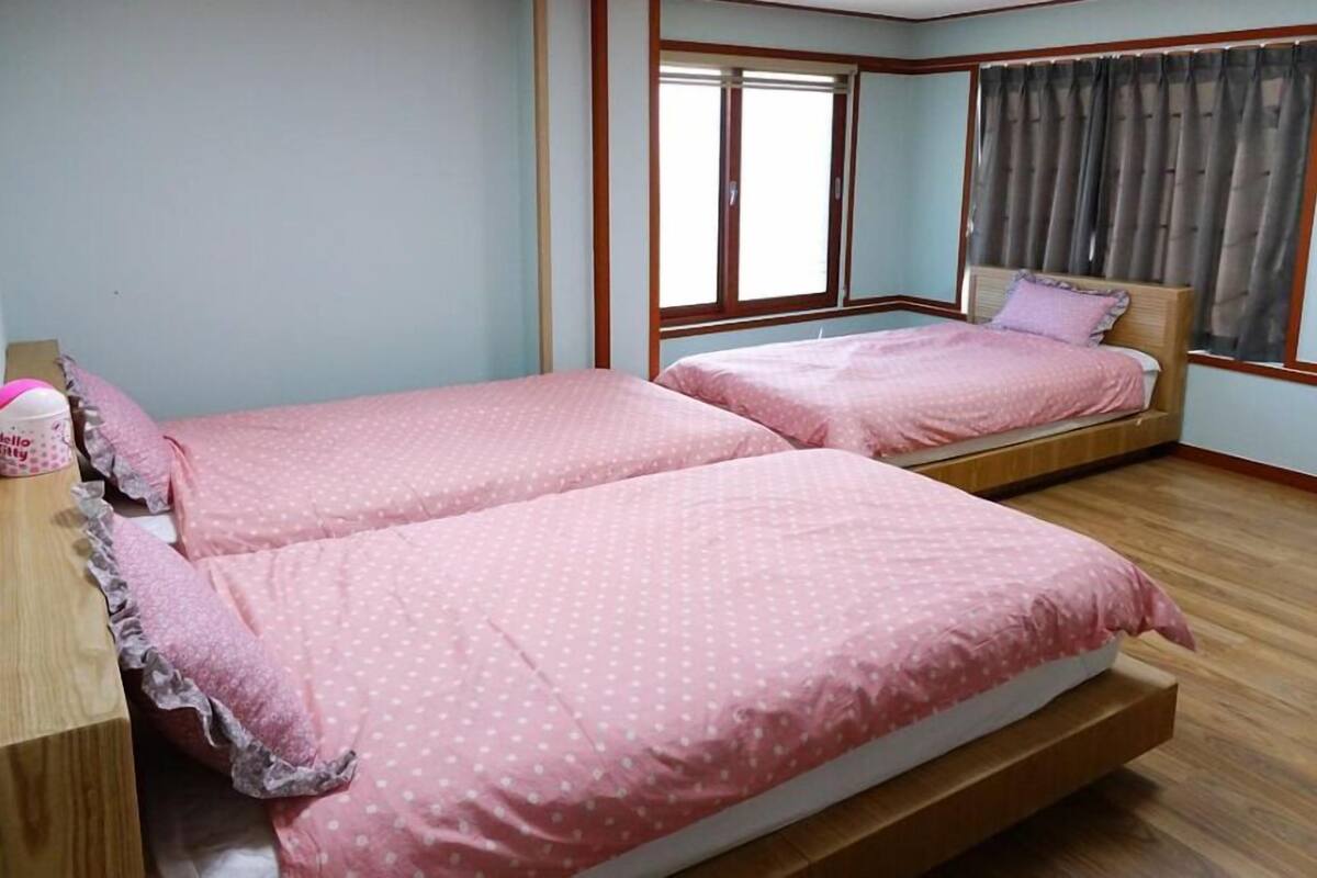 A bedroom with two beds, wooden flooring, and a window with curtains.