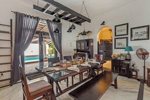 Un coin repas avec une longue table dressée pour quatre personnes, un banc en bois foncé et une vue sur une piscine grâce à une paroi en verre.