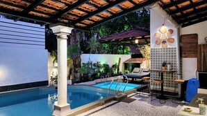 Ein privater Poolbereich mit Fliesen, Liegestühlen und einer überdachten Pergola.