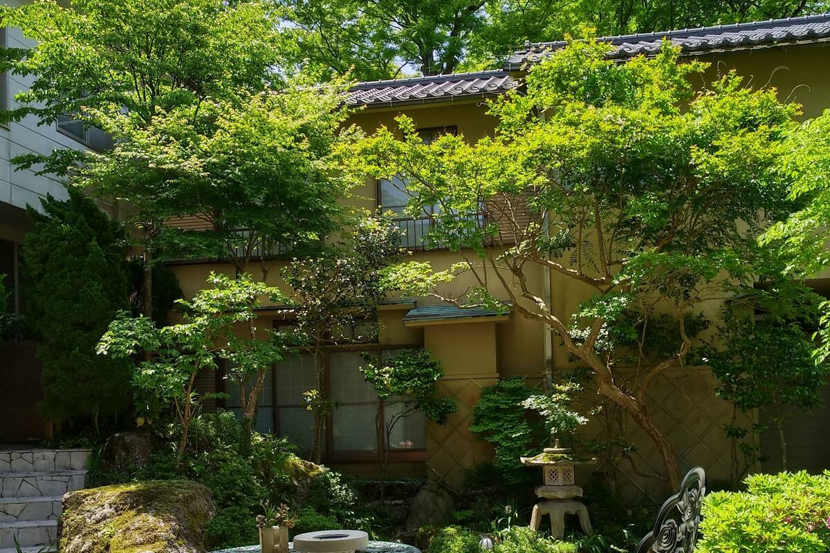 Eine Terrassensitzgelegenheit im Freien mit einem Steintisch und -stühlen, umgeben von üppigem Grün und einem Gebäude mit Ziegeldach.