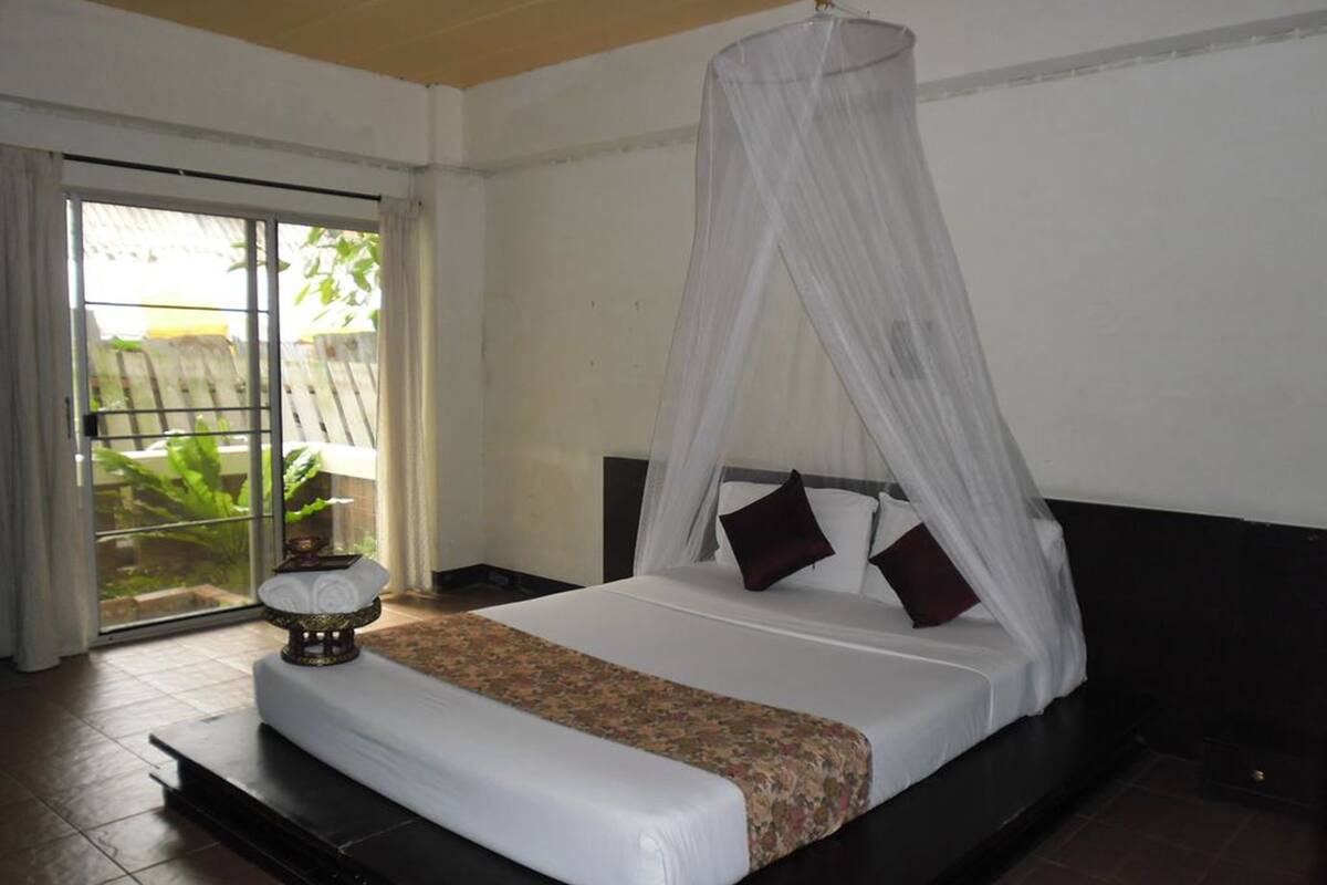 A bedroom with a bed, a canopy, a nightstand, and a view of the outdoors.
