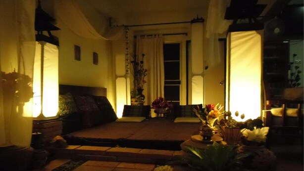 A cozy living room with a sofa, a coffee table, and a small table with flowers. There is a window with curtains and a door in the background. - Baan Pim (Chiang Mai)