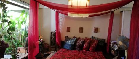 A bedroom with a bed, red curtains, a hanging light fixture, and a fan.