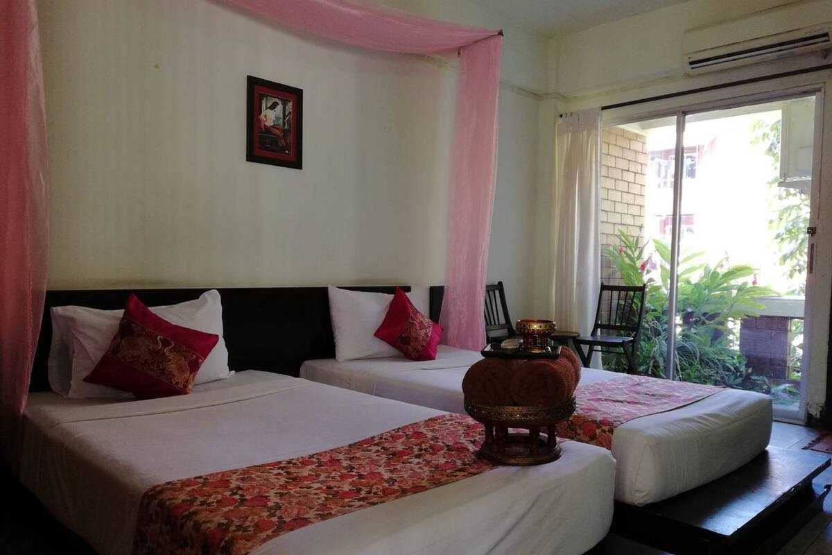 A hotel room with two beds, each with white linens and red floral bedspreads. There is a small table with a candle between the beds.