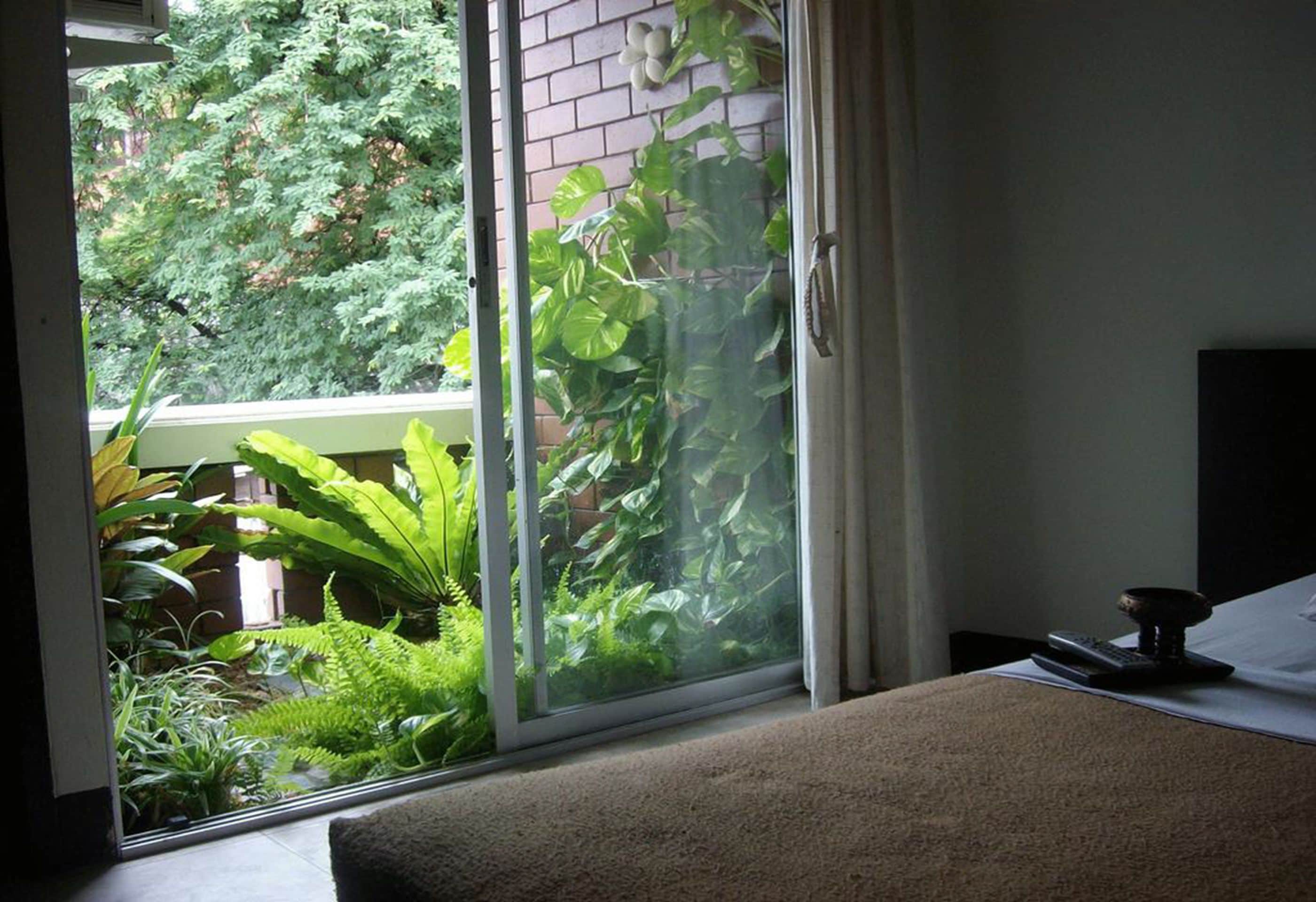 A room with a sliding glass door leading to a balcony with lush greenery.