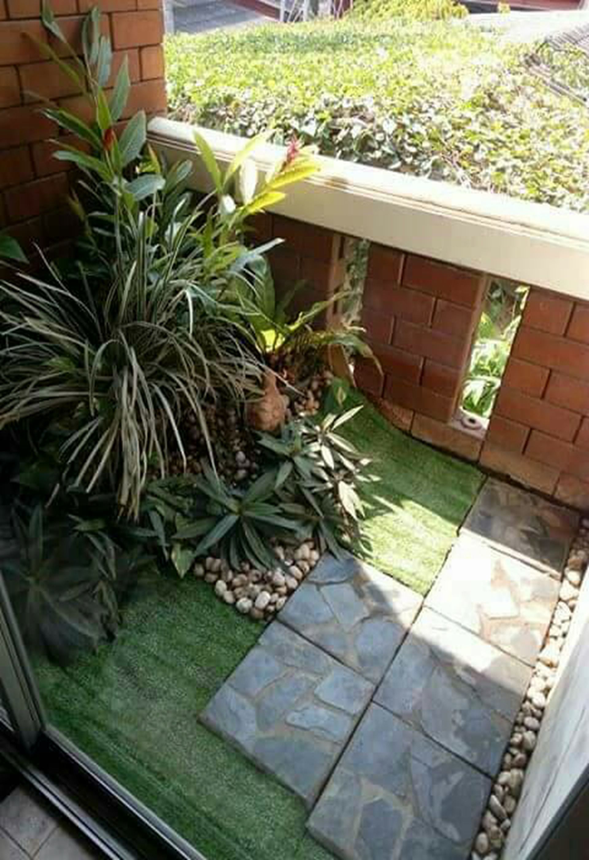 A small, enclosed outdoor area with a brick wall, a stone pathway, and various potted plants.