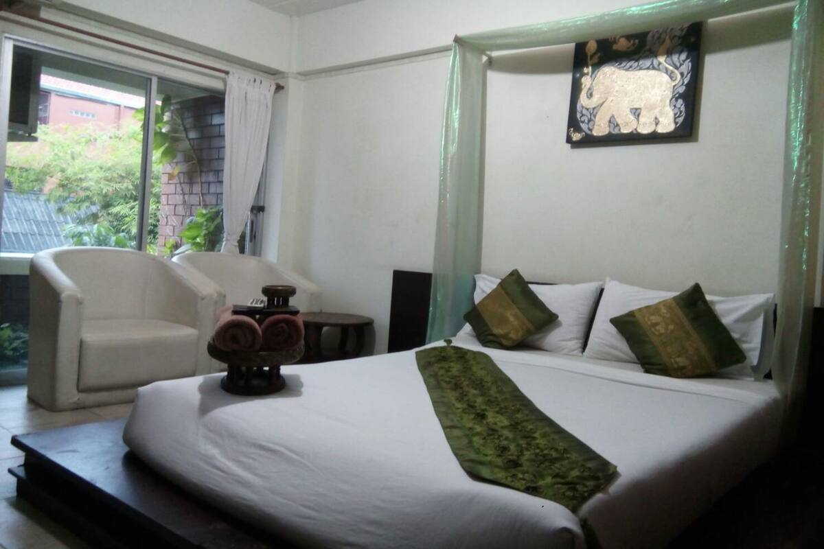 A hotel room with a bed, a chair, a small table, and a window with curtains.