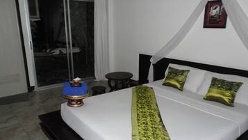Habitación de hotel con cama, una mesita, una silla y vistas al exterior mediante una puerta corredera.