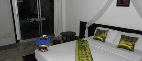 Ein Hotelzimmer mit Bett, kleinem Tisch, Stuhl und Blick durch eine Schiebetür nach draußen.