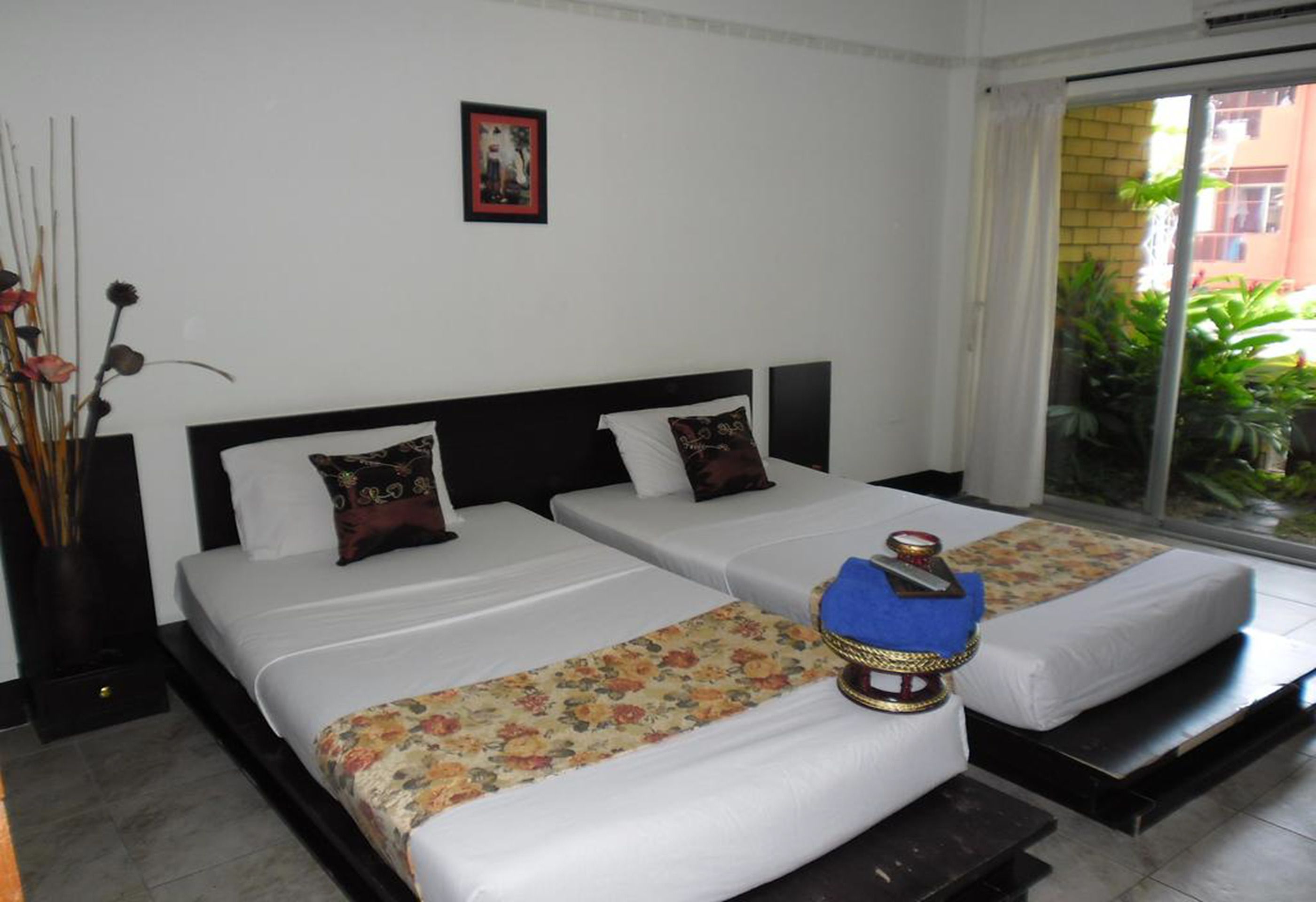 A hotel room with two beds, a large window, and a view of greenery outside.