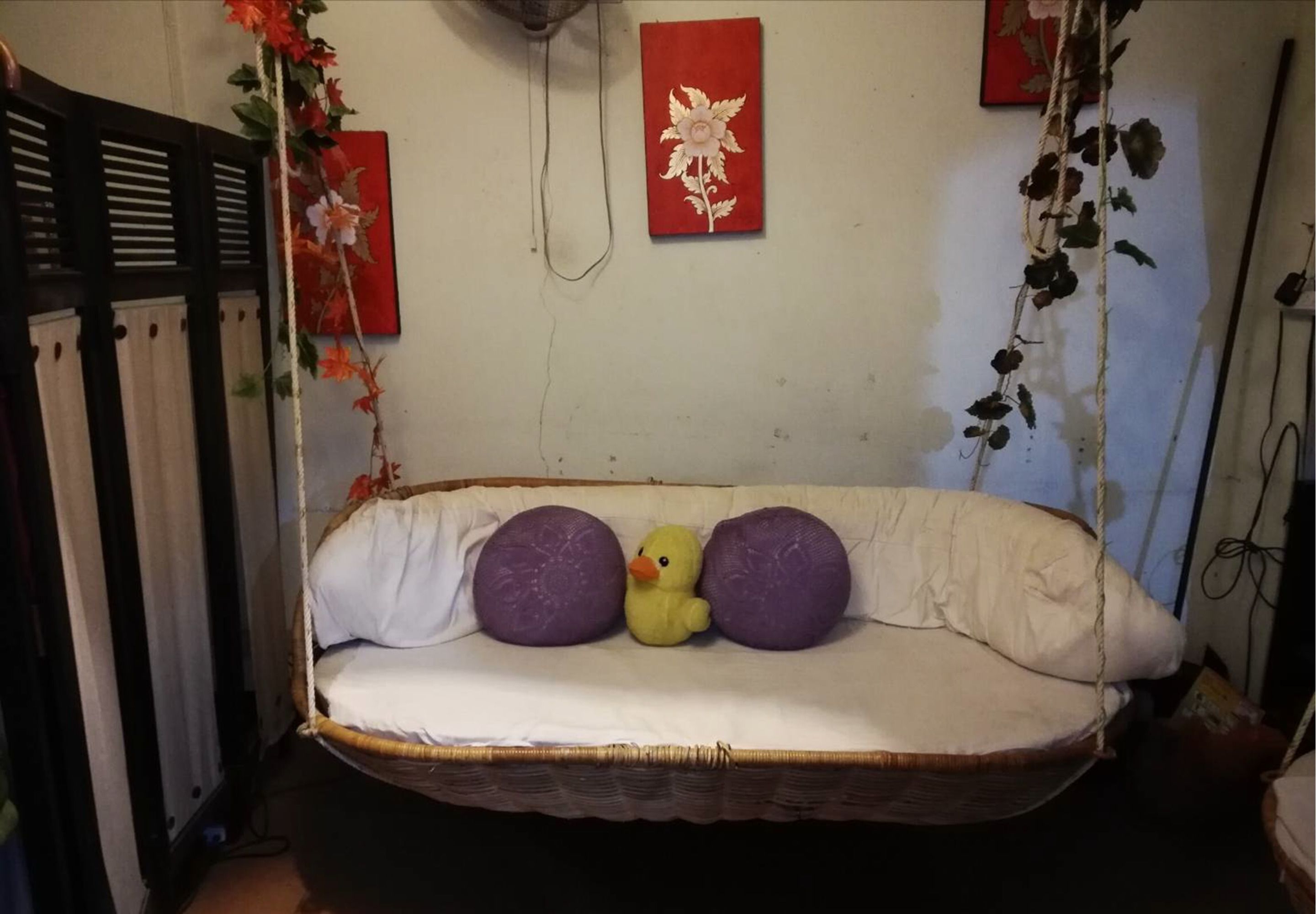 Ein Bett mit einer hängenden Schaukelstuhl, einer kleinen gelben Entenspielzeug und floraler Wandkunst in Rot.