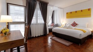 Habitació d'hotel amb llit, escriptori amb làmpada, cadira i finestra amb cortines.