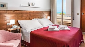 A hotel room with a wooden headboard, a bed with a red bedspread, a bedside table with a lamp, a phone, and a chair. - Casa Portofino Rooms&Breakfast (Cesenatico)