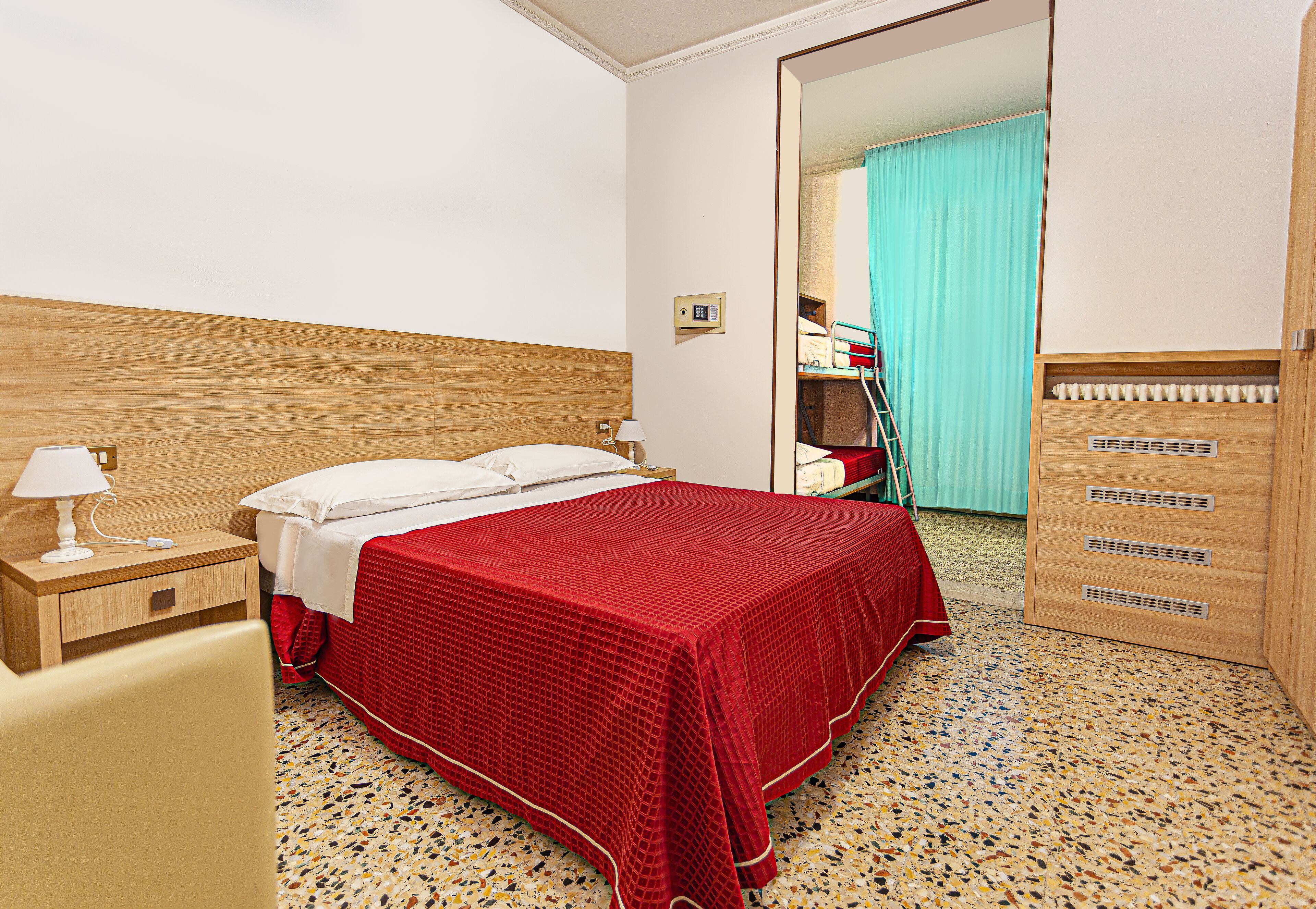 A hotel room with a bed, a nightstand, a dresser, and a mirror.