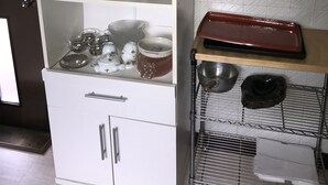Et køkken med hvide skabe, en metalkurv med skåle og et vindue med rullegardiner.
