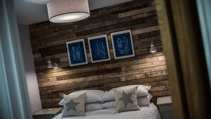 Un dormitorio con cabecera de madera, cama con ropa de cama blanca y almohadas estampadas con motivos de estrellas, y tres dibujos arquitectónicos azules enmarcados en la pared.