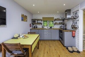 Una cocina compacta con armarios grises, un microondas y una estufa. Hay una mesa de comedor con sillas y un mantel amarillo.