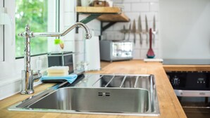 Cocina moderna con pileta de acero inoxidable, encimera de madera y ventana con vista a la vegetación.