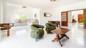 A spacious living room with a sofa, two green armchairs, a wooden coffee table, and a dining table. - Villa Irene - Amazing Villa with private pool near beach and golf course (Almancil)