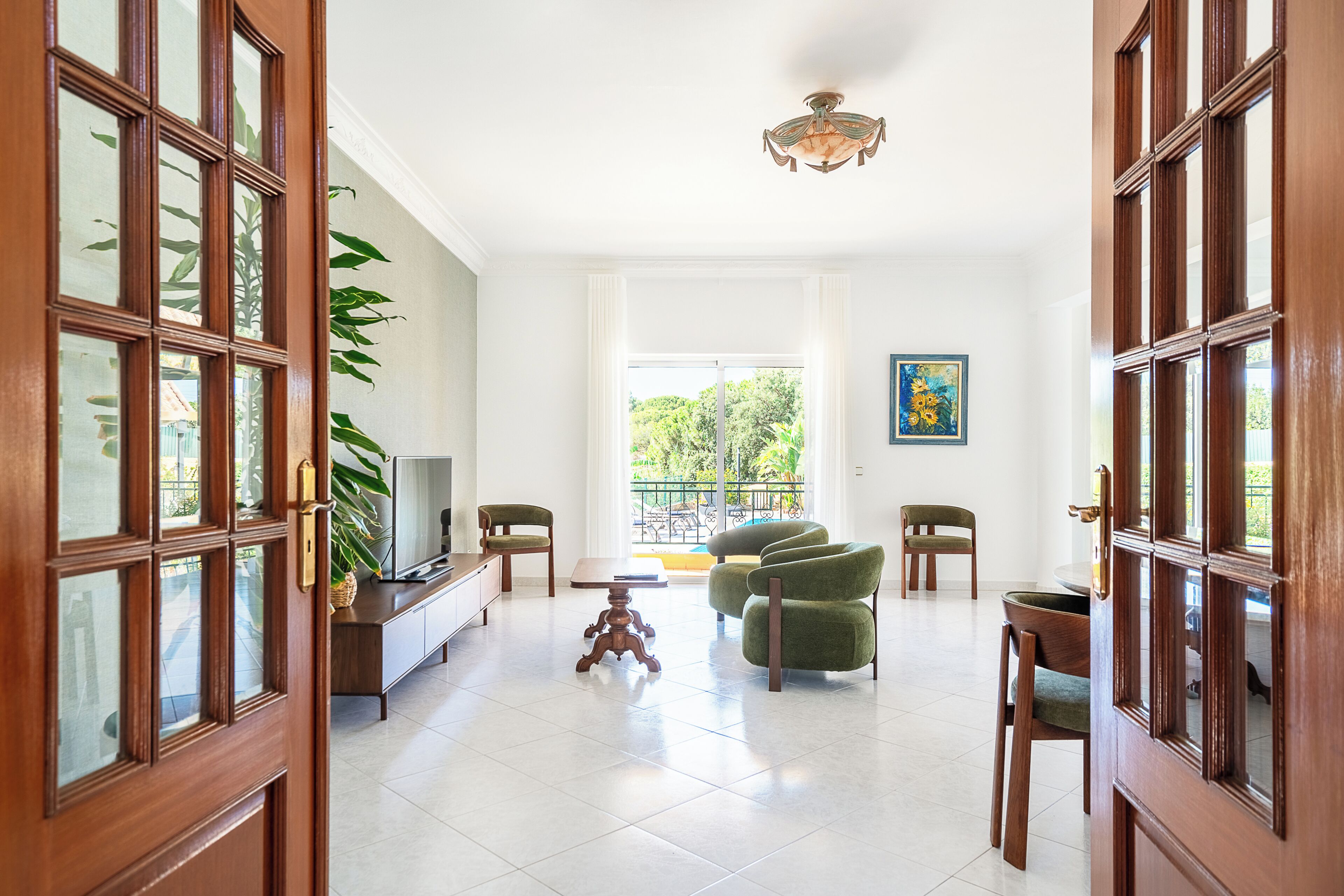 A spacious living room with a large window, a television, a dining table, and several chairs.