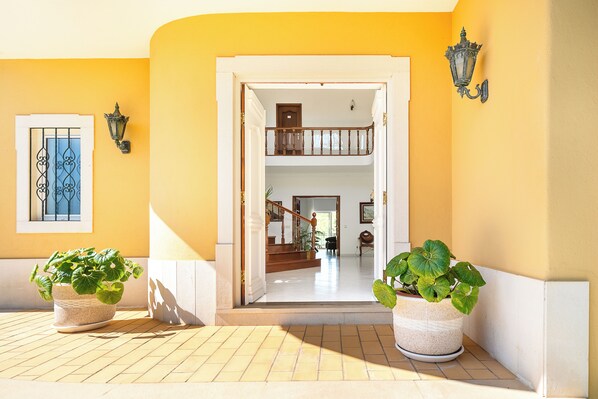 A hallway with a double door leading to a staircase and a room. There are two potted plants on the floor.