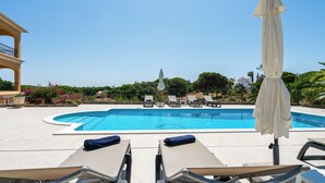 A pool area with lounge chairs and umbrellas, surrounded by greenery and buildings. - Villa Irene - Amazing Villa with private pool near beach and golf course (Almancil)