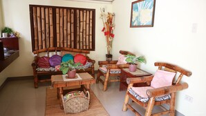 A cozy living room with a sofa, two wooden chairs, a small table, and a decorative bamboo screen. - Mabini Pensione (Puerto Princesa)